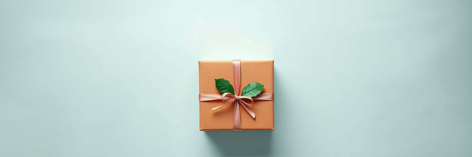 Gift box with ribbon and leaves placed on a light background ready for celebration occasions